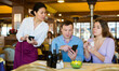 © JackF - Polite asian waitress taking order from couple sitting at table in restaurant. Guests choosing dishes from electronic menu in smartphones. Interactive restaurant ordering system concept