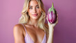 © Fox_Dsign - une femme tient une aubergine à côté de son visage avec un petit sourire évocateur