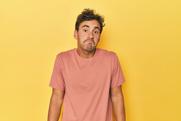 Wall Mural - Young Latino man posing on yellow background shrugs shoulders and open eyes confused.