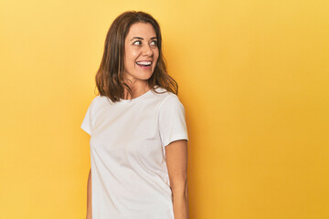 Wall Mural - Middle-aged caucasian woman on yellow looks aside smiling, cheerful and pleasant.