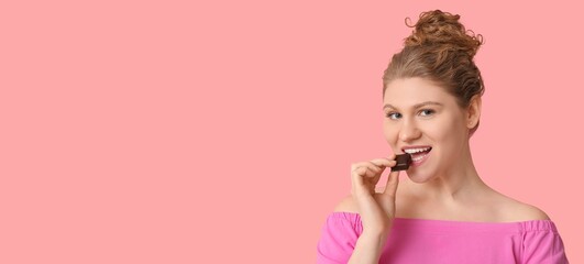 Wall Mural - Happy young woman eating chocolate on pink background with space for text