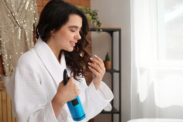 Poster - Pretty young woman applying hair spray on her curly hair in bathroom