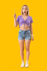 Poster - Shocked young beautiful woman with pen on yellow background