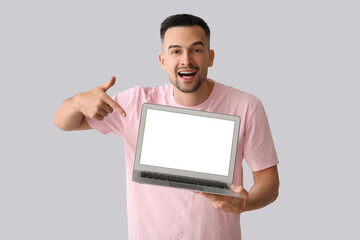 Wall Mural - Happy young man pointing at laptop on light background