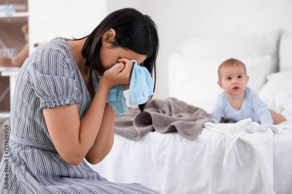 Crying young woman with laundry suffering from postnatal depression in bedroom
