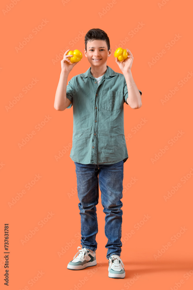 Cute little boy with bell peppers on orange background