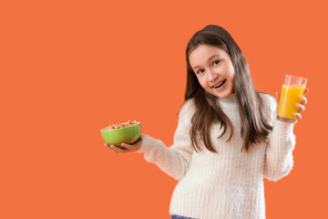 Canvas Print - Cute little girl holding bowl with cereal rings and glass of juice on orange background