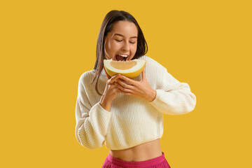 Wall Mural - Young woman eating pomelo slice on yellow background