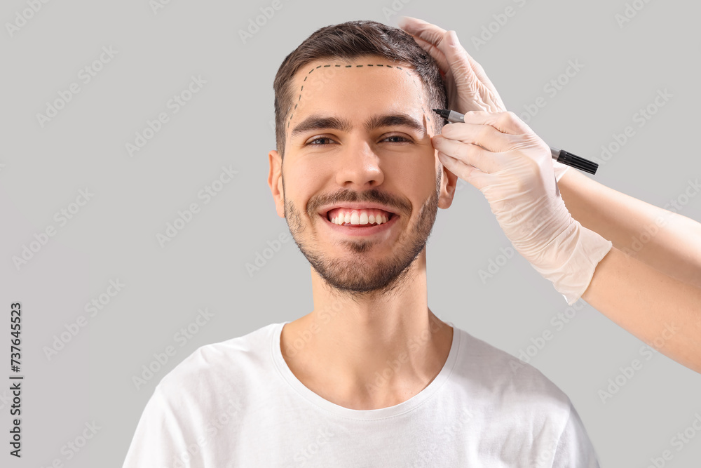 Doctor marking young man's forehead with hair loss problem on light background, closeup