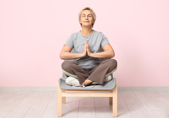 Sticker - Portrait of meditating mature woman sitting on chair against pink wall