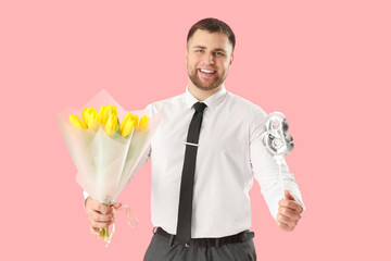 Wall Mural - Handsome man with bouquet of flowers and balloon in shape of figure 8 on pink background. International Women's Day celebration