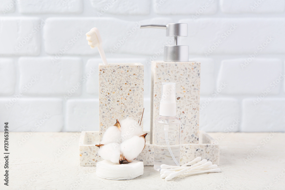 Composition in white color with cotton buds and tooth brush on table near brick wall. Bath accessories