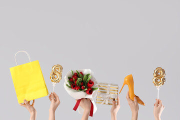 Female hands with bouquet of red tulips, gift box and shopping bag on white background. International Women's Day