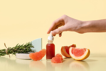 Wall Mural - Female hand with bottle of essential oil, rosemary and ripe grapefruit on color background, closeup