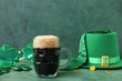 Mug of dark beer with leprechaun hat, tie and plastic eyeglasses for St. Patrick's Day celebration on green grunge background