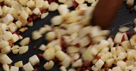 Canvas Print - Cooking potato hash with bacon and prosciutto in a skillet, stirring with a wooden spoon