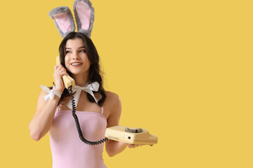 Wall Mural - Sexy young woman in bunny costume talking by telephone on yellow background. Easter celebration