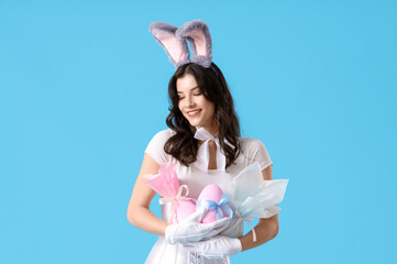 Wall Mural - Sexy young woman in bunny costume with Easter gift eggs on blue background