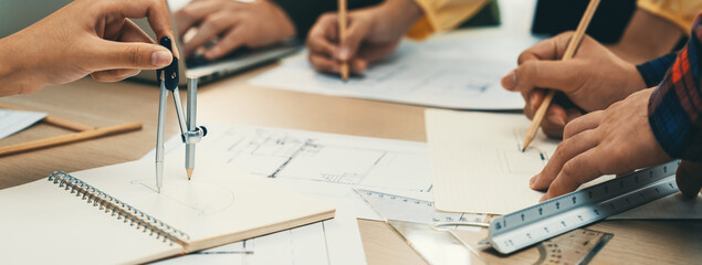 Skilled architect team using architectural equipment during colleague discussion about building design at meeting table with blueprint scatter around. Closeup. Focus on hand. Delineation.