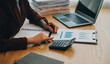 © ARMMY PICCA - Asian Businesswoman Using laptop computer and working at office with calculator document on desk, doing planning analyzing the financial report, business plan investment, finance analysis concept.