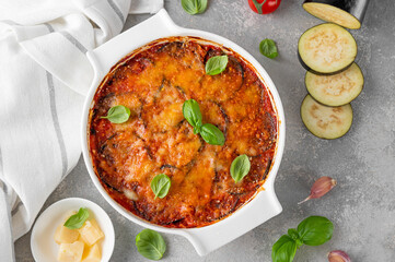 Wall Mural - Eggplant casserole with cheese and tomato sauce in a white baking dish on a gray concrete background with ingredients for cooking. Vegetarian healthy food.