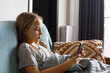 © millaf - Pretty child girl looking using and touching mobile phone screen on sofa. Kid smiling and using  smartphone. Cute girl watching videos while tv, Internet addiction.