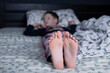 Bare feet of a child. A child in pajamas. Bare feet sticking out from under the blankets. The boy is sleeping in bed. Foot and leg
