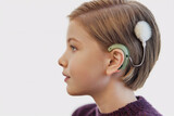 Fototapeta Sawanna - Teen girl with blond hair wearing cochlear implant cover of a fluffy hairpin.