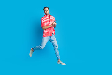Poster - Full size photo of intelligent man dressed striped shirt denim pants run empty space hold smartphone isolated on blue color background