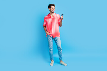Poster - Full body photo of clever cheerful guy wear stylish shirt jeans trousers look at smartphone read email isolated on blue color background