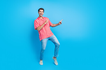 Wall Mural - Full size photo of optimistic man dressed striped shirt denim pants indicating at sale empty space isolated on blue color background