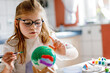 © Irina Schmidt - Little girl painting globe or ball with colors. School child making earth globe for school project. Happy kid with eyeglasses holding brush.
