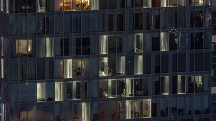 Wall Mural - Frontal view of night facade of tower building with a lot of windows in apartments with light timelapse. Life in every window. Aerial view of the glass facade of an office and residential skyscraper.