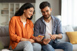 © Home-stock - Family shopping online. Happy indian spouses using cellphone and credit card, making payment in store via phone, sitting on sofa at home