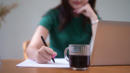 Young asian student women using technology laptop to studying and watching lecture webinar in online class while writing information in notebook and learning knowledge remote education from home