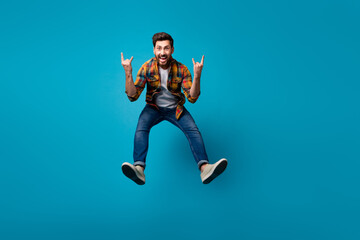 Sticker - Full size photo of handsome young male jump show rock horns symbol dressed stylish checkered outfit isolated on blue color background