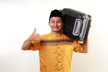 Happy asian muslim man carrying travel suitcase while showing thumbs up gesture. Going mudik or travel to hometown for Ramadan eid mubarak celebration