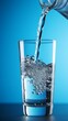 Pouring fresh water into a clear glass against a blue background. Dynamic splash and bubbles as water fills a drinking glass.