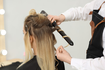 Wall Mural - Hair styling. Hairdresser curling woman's hair in salon, closeup