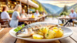 Fisch mit Salzkartoffeln, im Hintergrund Restaurant Terrasse mit Gästen 