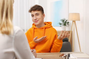 Psychologist working with teenage boy at table in office