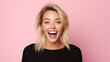 a beautiful blonde woman wearing black shirt expressing happiness emotion with her mouth laughing and big wide open eyes. isolated on pink background