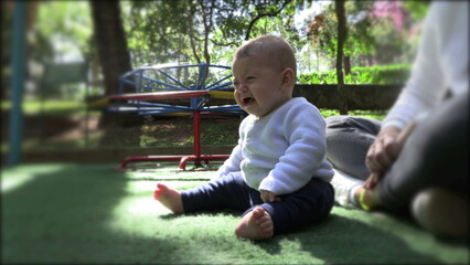 Wall Mural - Upset baby toddler seated at playground park outdoors