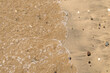 Ola y arena mojada por el efecto de las olas en la playa. Arena y pequeños cantos rodados arrastrado por la marea en la cala de Enmedio en Níjar, Almería, España.