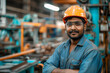 Confident Engineer with Arms Crossed in Manufacturing Plant. A young confident engineer wearing a hard hat and safety vest with arms crossed in a manufacturing plant.