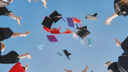 Graduates tossing multicolored hats against a blue sky.
