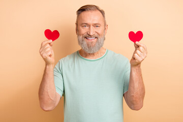 Photo of positive nice retired man wearing trendy clothes demonstrating two hearts isolated on beige color background