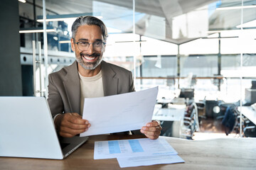 Wall Mural - Happy mature professional business man lawyer holding documents in office. Middle aged male ceo executive, entrepreneur or bank manager sitting at desk in corporate office. Portrait, copy space.