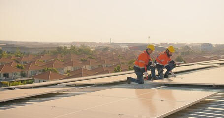 Two engineers solar technicians in reflective gear discussing working examine solar installations on rooftop panels at dusk, with suburban backdrop