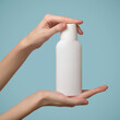 A woman's hands holds a white bottle of shampoo. Template blank copyspace. Blue background.
